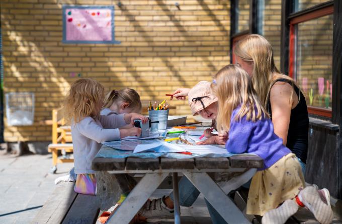 Børn og pædagog sidder og tegner på legepladsen i Bistrup Have